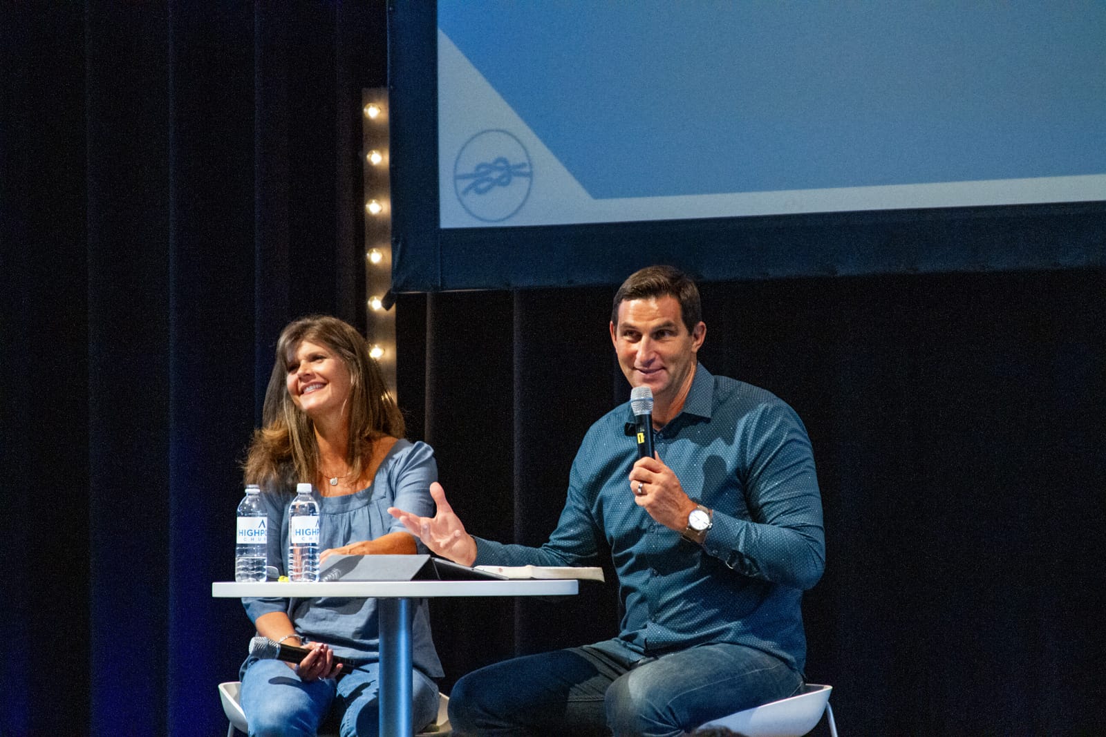Ron and Jody sitting on high chairs presenting at a conference
